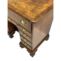 Early 18th century Queen Anne figured walnut kneehole desk with secretaire drawer, moulded and book matched top with walnut band, the top drawer with fall front enclosing small drawers and pigeon holes, fitted with nine drawers and central recessed cupboard, on ogee bracket feet