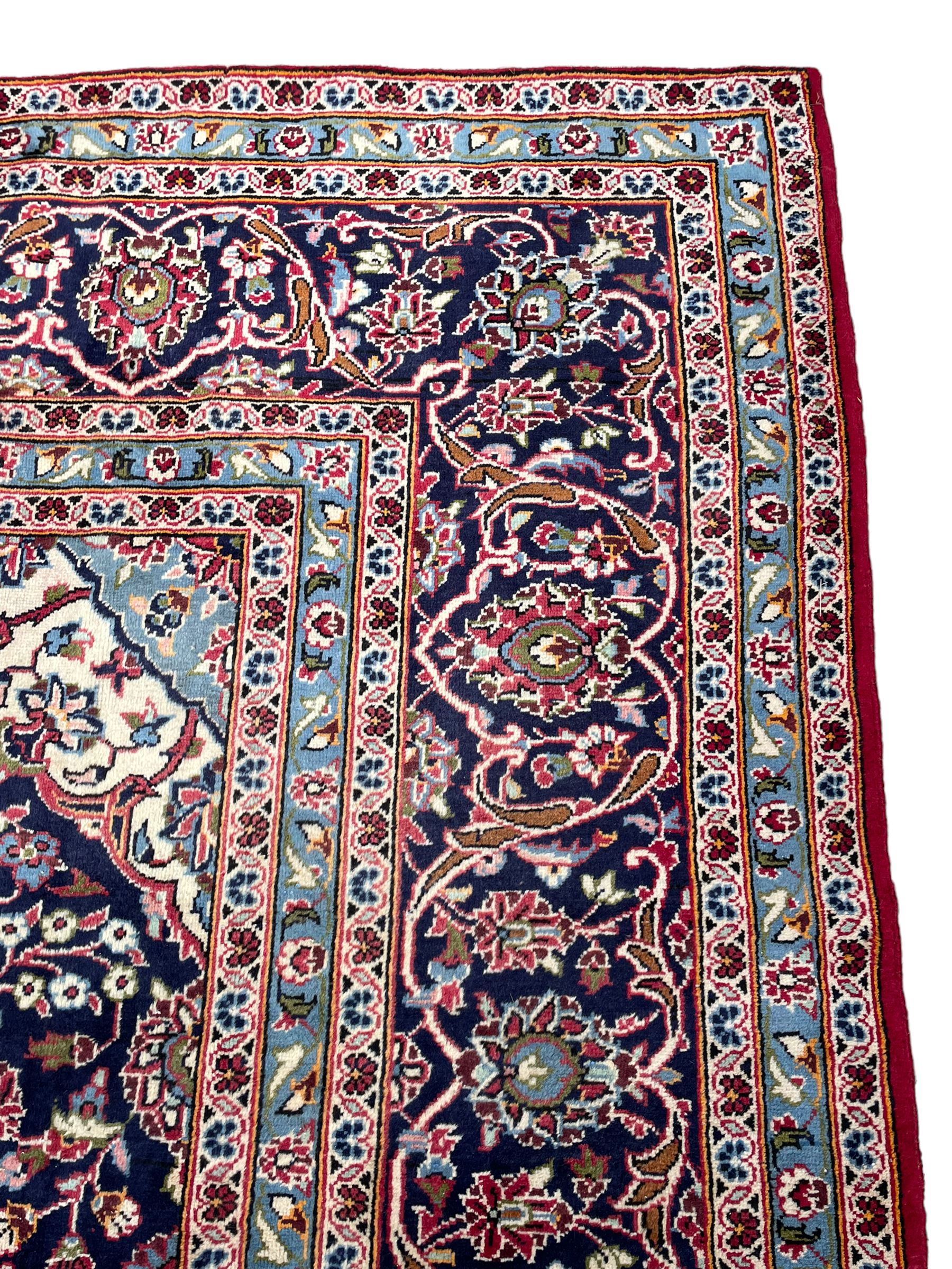 Central Persian Kashan crimson ground carpet, central  floral pole medallion with matching spandrels within a field of scrolling palmette motifs and foliage, the heavily banded indigo border with repeating plant motifs interlaced with scrolled branches