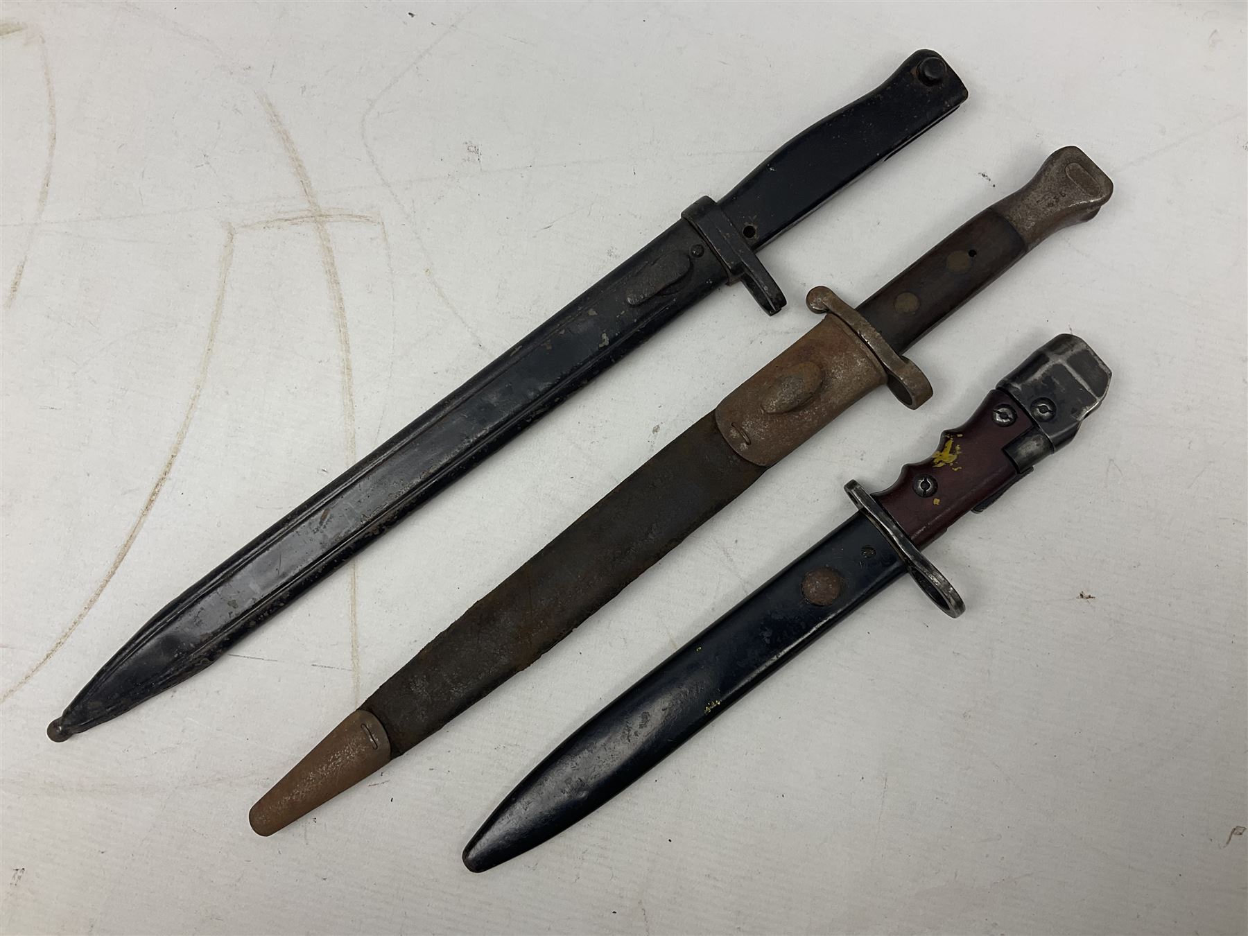 British No 7 MKI knife bayonet with 20cm single edged fullered clipped point blade;  blackened steel, large muzzle ring cross-guard; blackened swivelling pommel marked 'F5H'; red Tufnol composite grips; in blackened steel scabbard L33cm overall; British Pattern 1888 bayonet with scabbard; and German Ersatz bayonet with scabbard (3)