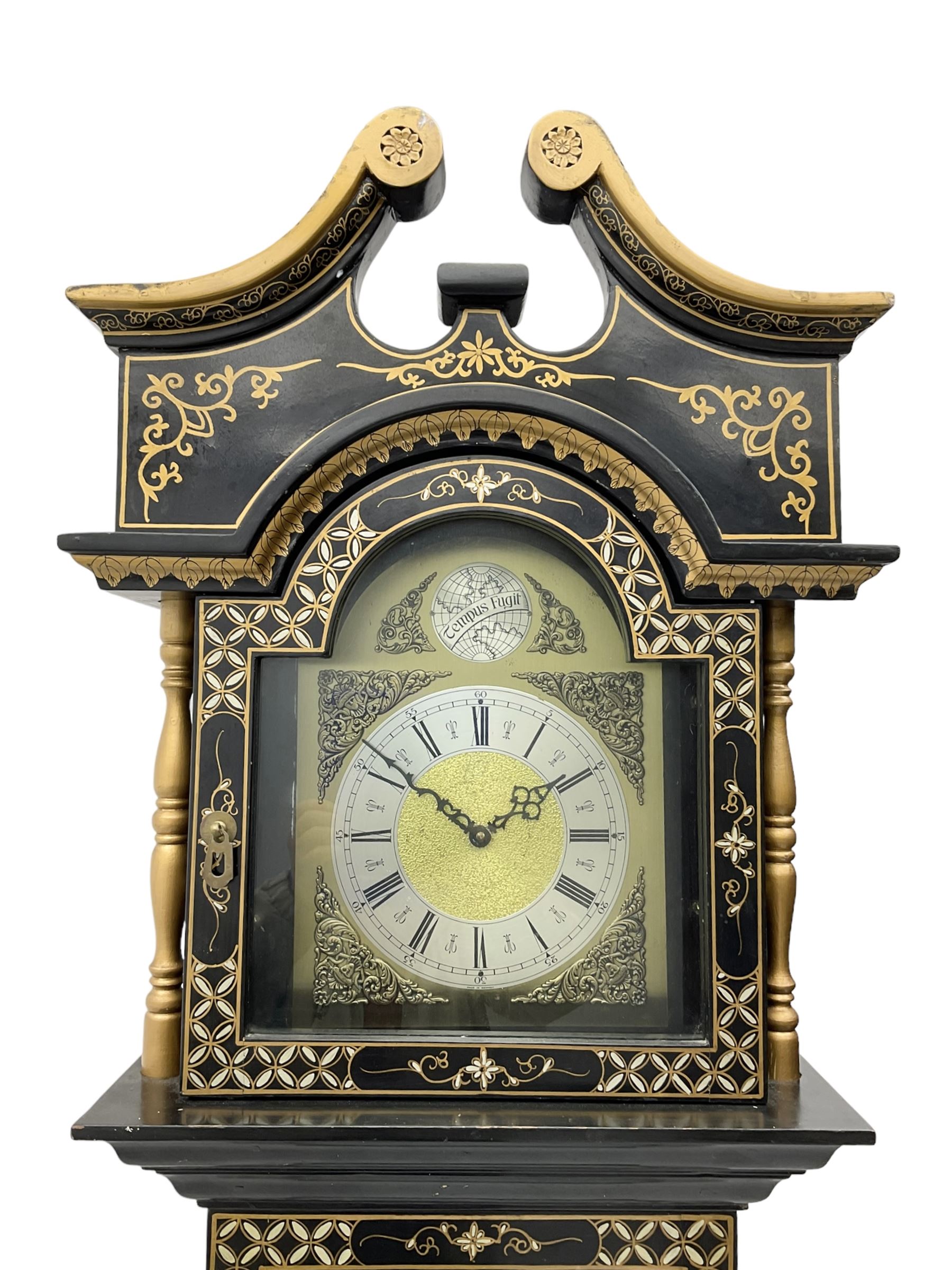 20th century 8-day chain driven black lacquered longcase clock - with a swans neck pediment and break-arch hood door, fully glazed trunk door displaying brass cased weights and pendulum, case sides, hood and plinth profusely decorated in gold relief and chinoiserie figures, brass break arch dial with an etched centre and silvered chapter ring, German two train movement striking the hours and half hours on two gong rods. With weights and pendulum.
