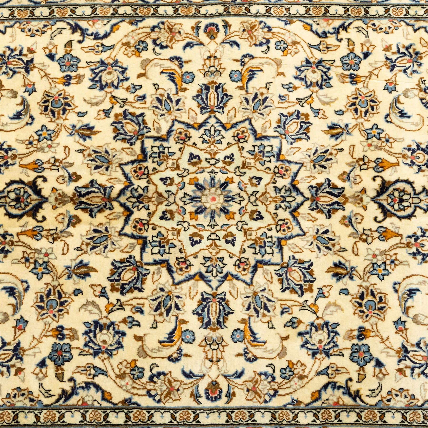 Central Persian Kashan hand-knotted rug, ivory ground, with a small central floral medallion and pendants, the field decorated with fine blue, ochre and beige scrolling vines, flowerheads and palmettes, within an ivory border of repeating floral sprays and meandering vines, flanked by narrow guard stripes, with cotton fringes