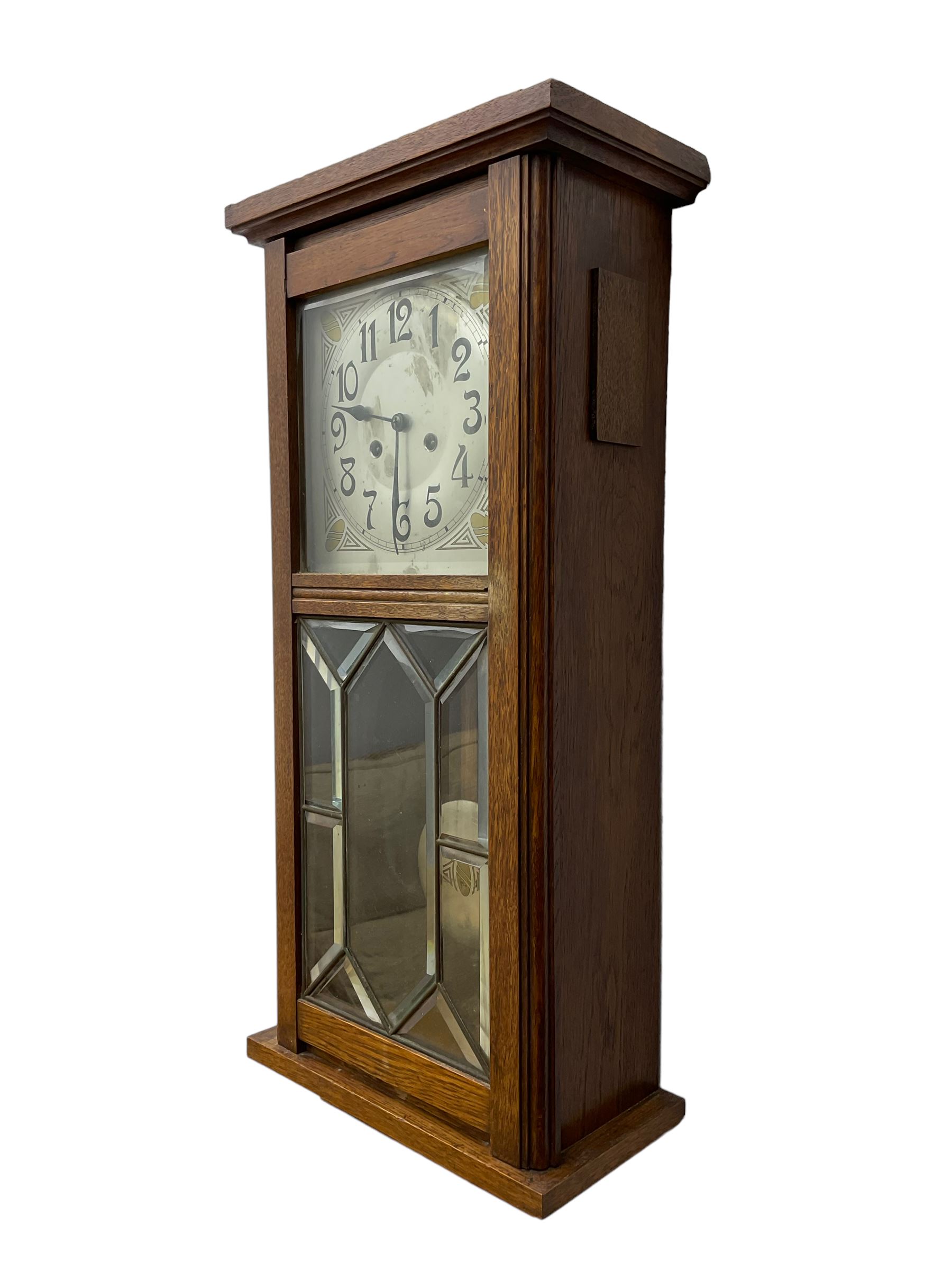 German - Art Deco oak cased 8-day wall clock c 1930, with a moulded flat top and fully glazed door, deeply cut bevelled glass panels and visible pendulum, silvered dial with Art Deco design spandrels, Arabic numerals, minute track and spade hands, twin train movement striking the hours and half hours on four gong rods. With pendulum and key.  