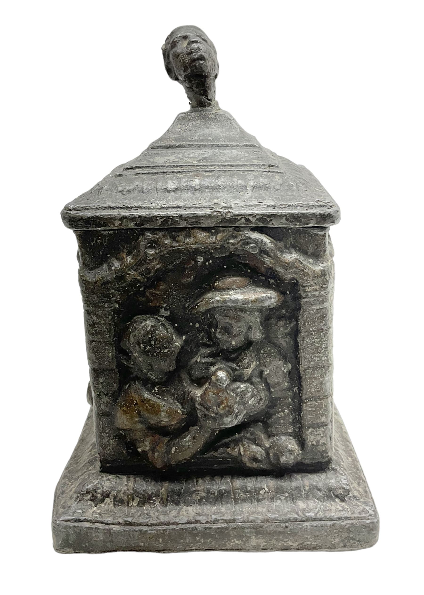 19th century lead tobacco box, the body of square form decorated with panels of courting couples in relief supporting stepped tapering lid with figural male head finial, H18.5cm