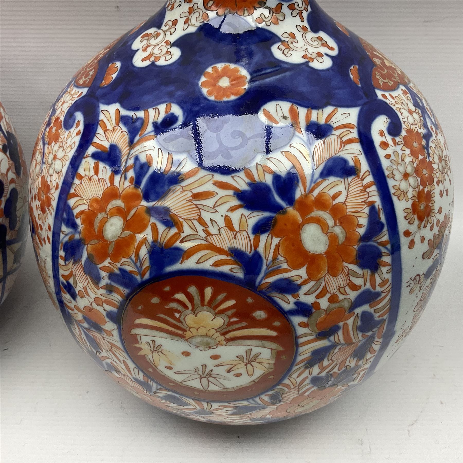 Pair of large 19th century Japanese Imari porcelain bottle vases, painted with shaped reserves of peonies, chrysanthemums and prunus blossom, each H46cm