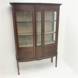  Edwardian inlaid mahogany shaped front display cabinet, projecting cornice, two glazed doors enclosing lined interior with two shelves, square tapering supports on spade feet, W122cm, H179cm, D46cm  