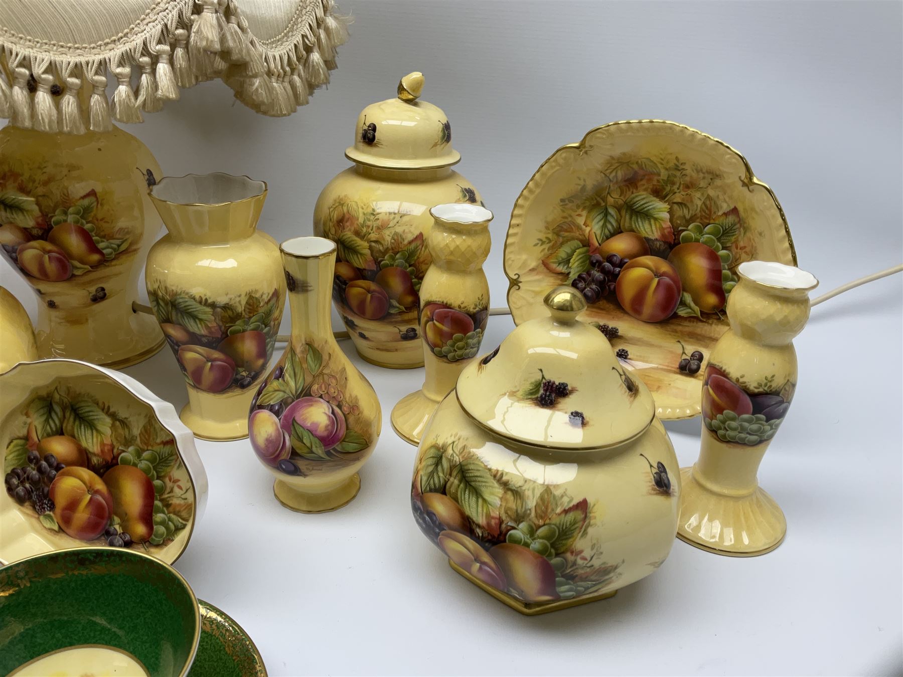 Collection of Aynsley Orchard Gold pattern wares, comprising lamp base, three jars and covers, six vases or various size and form, large jug, lidded dish, pair of cruets, pair of candlesticks, mug, two pin dishes, lobed dish, tea cup, saucer, size plate, and cake plate, and two further cups and saucers, each cup decorated with central Orchard Gold reserve to the interior against a mottled pink or green ground. 