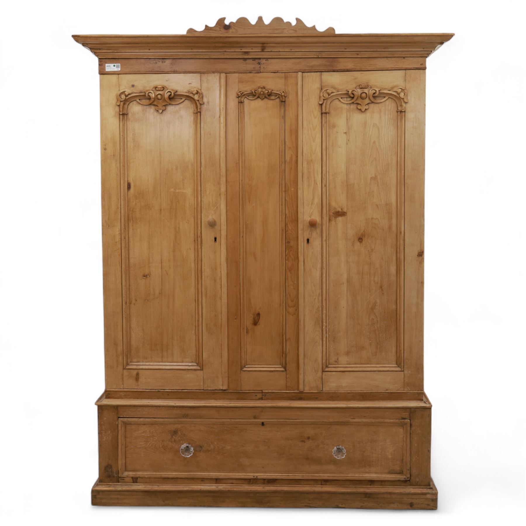 Late 19th century pine wardrobe, with stepped cornice over triple panelled doors, applied foliate carvings to outer panels, raised over a separate pine plinth drawer with moulded facia and twin glass pulls
