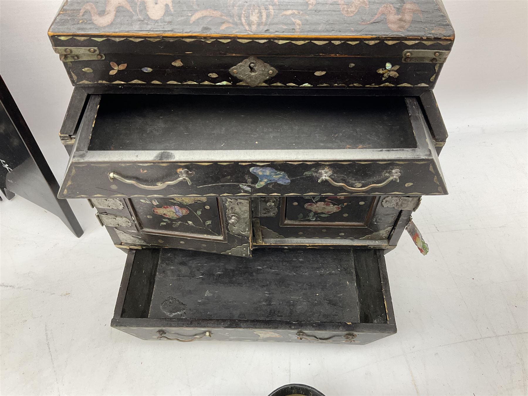 Late 19th / early 20th century Japanese lacquered table top cabinet, heavily decorated with mother of pearl inlay depicting blossoming branches, flowers and birds, the two hinged doors between longer drawers opening to reveal interior fitted with four short drawers, with lift up hinged canted lid, H28cm D9.5cm W23cm, together with mother of pearl inlaid miniature folding screen, dish decorated with walking figures with crimped edge, boxes decorated with flowers, birds and gilt etc
