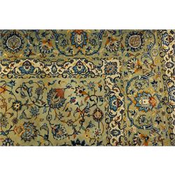Central Persian Kashan hand-knotted carpet, pale blue field decorated with a finely drawn all-over scrolling floral vine design incorporating stylized palmettes, rosettes and foliate sprays, with a small central circular medallion, enclosed by a conforming floral vine border between multiple guard stripes, with cotton fringe ends  