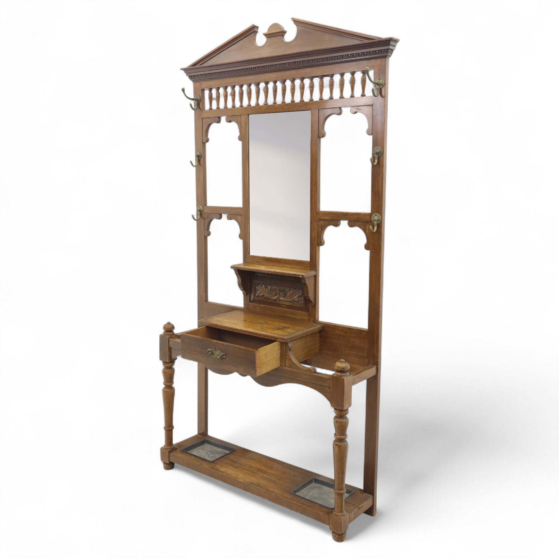 Edwardian walnut hall stand, the shaped pediment above turned spindle gallery and bevelled mirror, fitted with brass double coat hooks, single drawer with cast handle and carved frieze, flanked by turned supports, lower platform fitted with twin metal drip trays