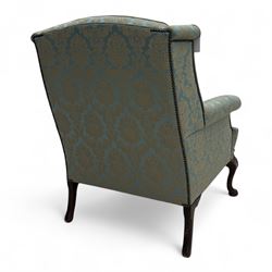 Georgian design carved walnut framed wingback armchair, upholstered in pale blue and gilt floral damask, with shaped loose seat cushion and rolled arms, raised on scallop and cartouche carved front cabriole supports terminating to pad feet