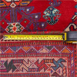 South West Persian Qashqai hand-knotted runner, madder red field  with central vertical succession of stepped lozenge medallions enclosing angular tribal devices and stylized floral motifs, principal medallion in deep indigo with ivory and sky blue highlights, field densely scattered with small geometric ornaments, hooked elements and zoomorphic forms, triangular indigo spandrels enclosed within multiple narrow guard stripes and principal border, with cotton fringe ends 
