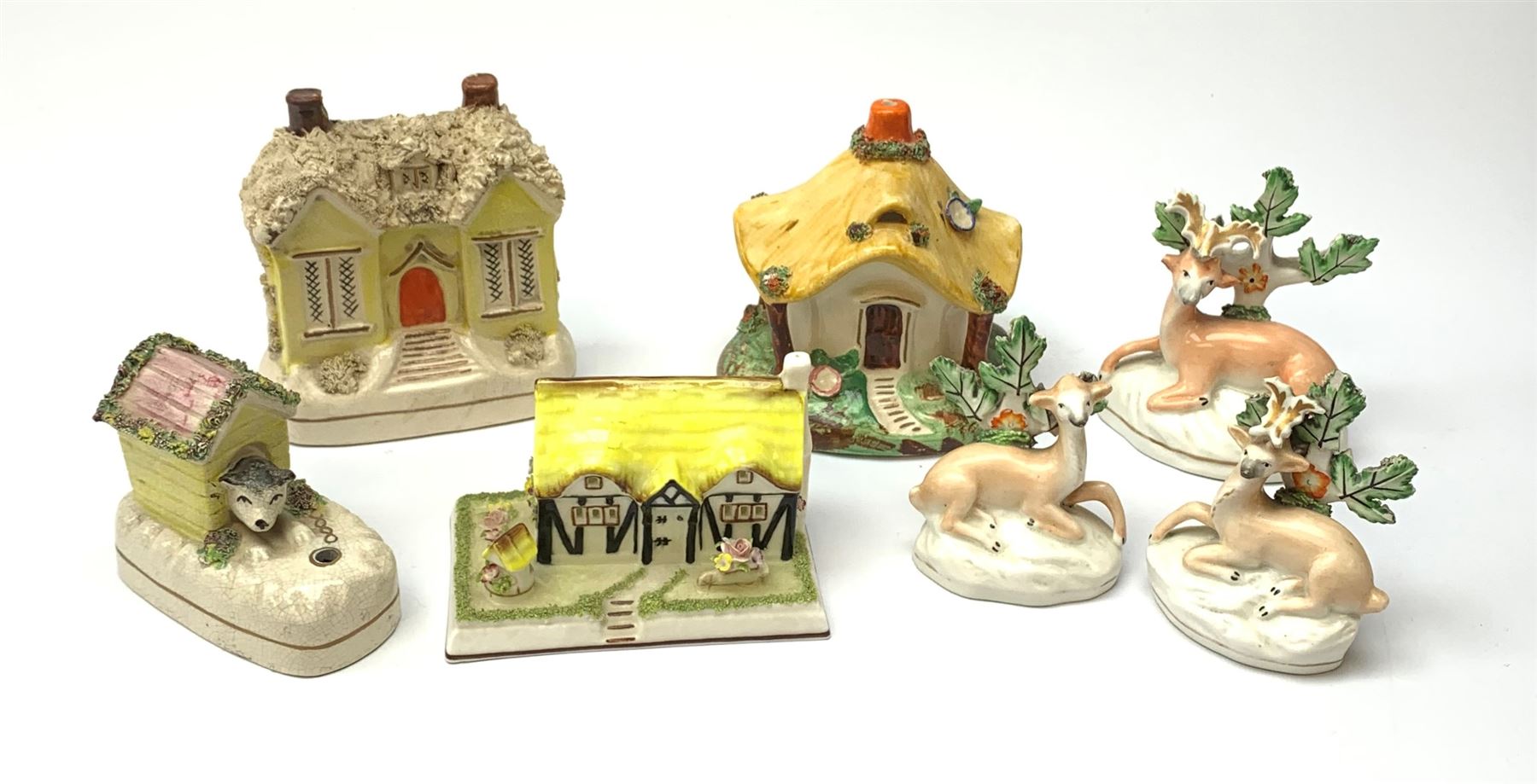 A group of Victorian and later figures, comprising Victorian Staffordshire money box in the form of a house, a Victorian Staffordshire pastille burner in the form of a house, three figures modelled as recumbent deer before trees, Staffordshire style model of a dog emerging from a kennel upon pen holder base, and Coalport pastille burned in the form of a house. (7). 