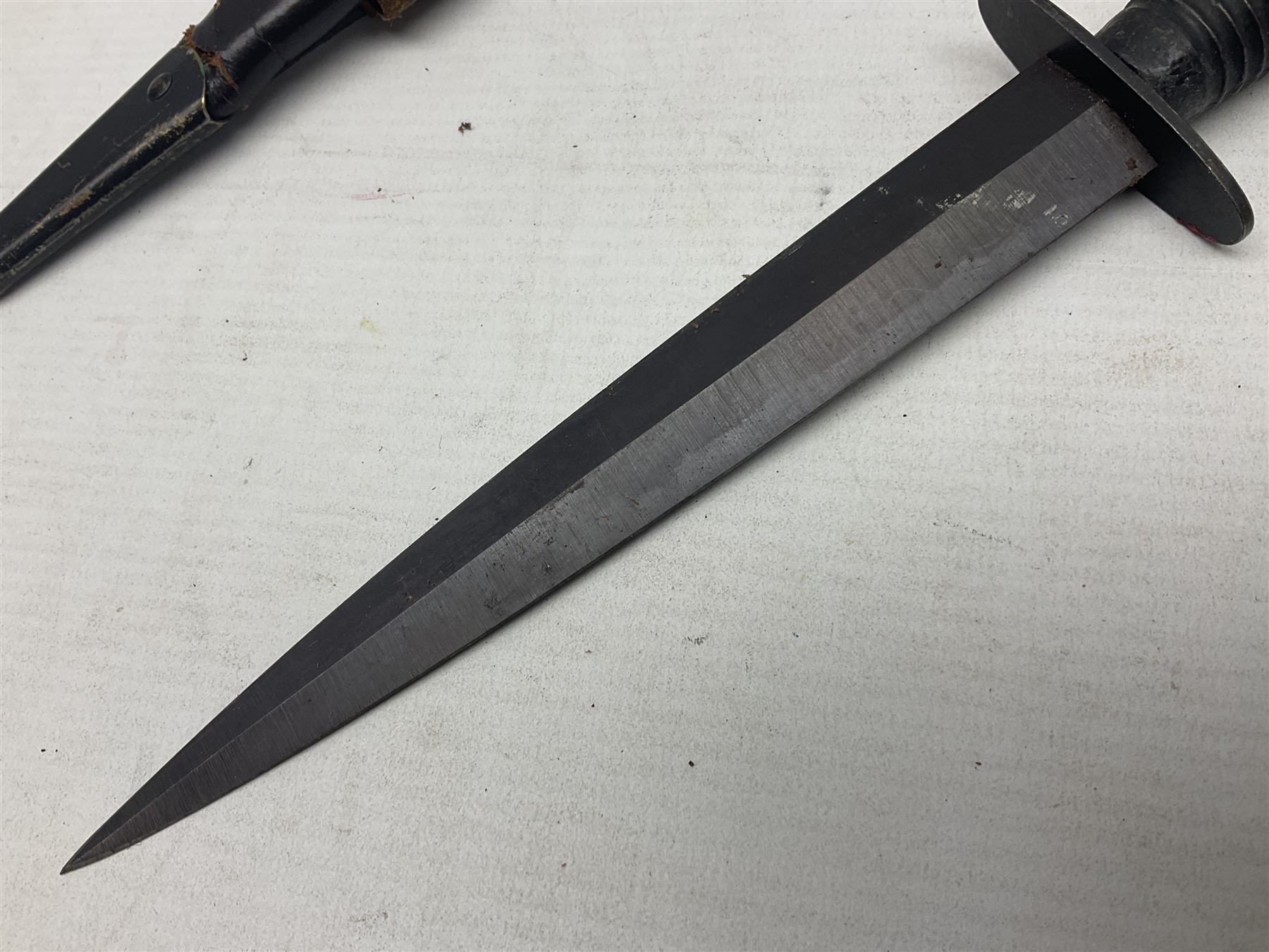 Third Pattern Commando Knife or Dagger with 17.5cm flattened diamond section blade and regulation black painted ribbed copper hilt with brass pommel nut; stamped William Rodgers Sheffield England to the cross-piece; in black painted brass mounted leather scabbard L34.5cm overall