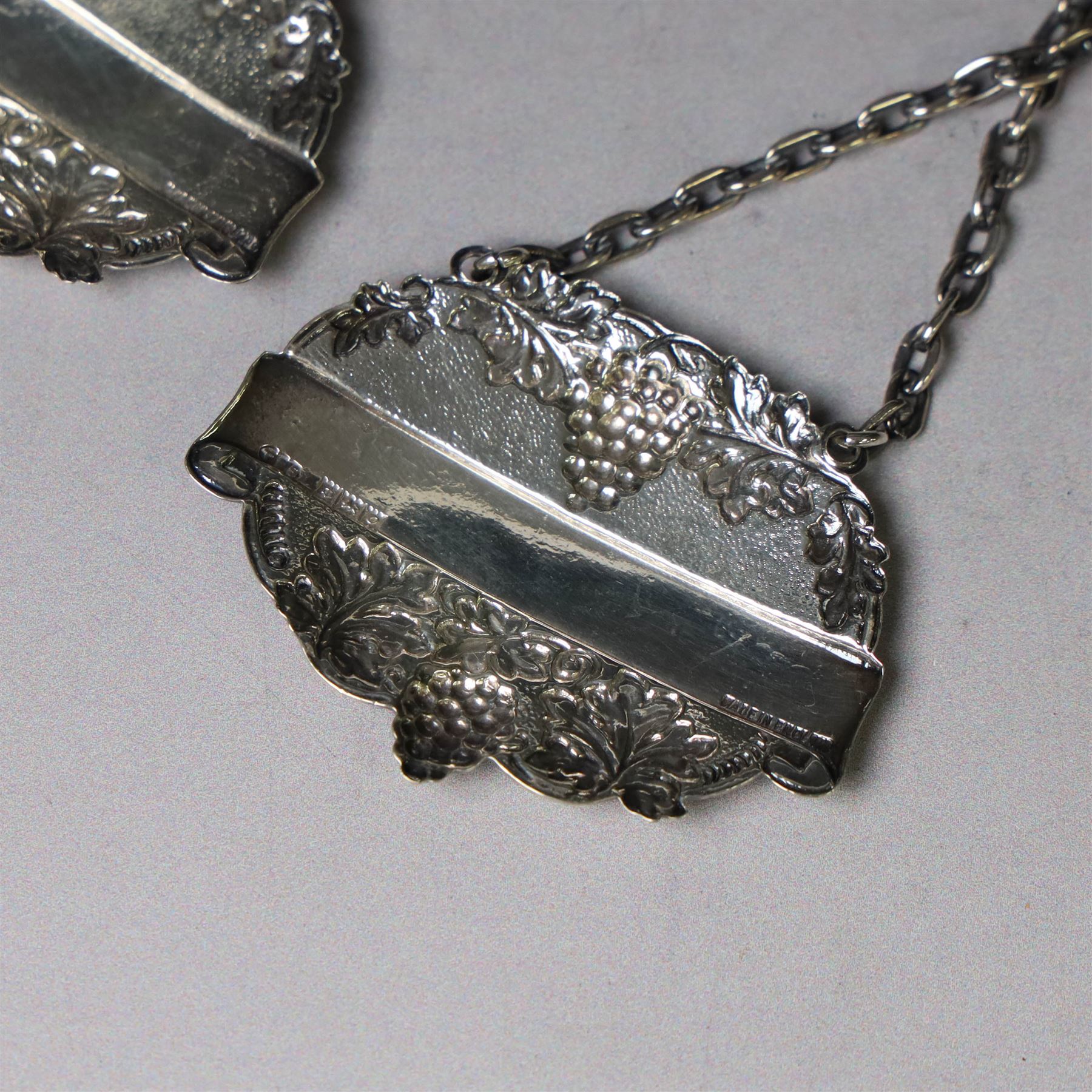 Silver bottle coaster, of circular form with turned wooden centre and pierced sides, hallmarked LGS, London 1977, together with two decanter labels, each with embossed grape vine decoration engraved Scotch and Sherry, hallmarked 