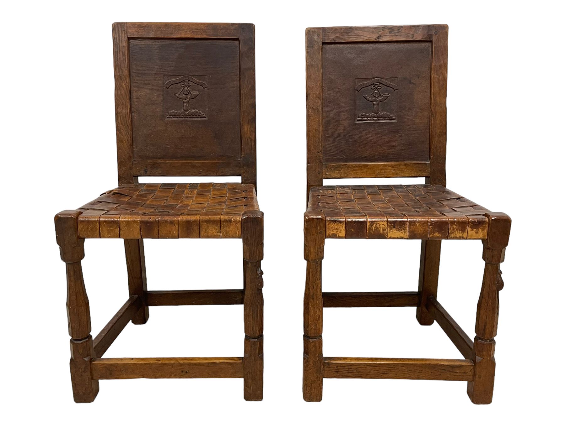 Mouseman - circa. 1930s set of six (4+2) oak dining chairs, panelled back carved with the Bagshawe family crest, the moto 'Forma Flos Fama Flatus' over an arm grasping a bugle-horn with ribbon tie and Yorkshire rose motif, adzed frame, leather lattice strap seat, on octagonal supports united by stretchers, two carvers and four side chairs, each carved with mouse signature, by Robert Thompson of Kilburn 

Provenance: Owned since manufacture by the Bagshawe family, descendants of the Staithes Group Artist Joseph Richard Bagshawe RBA (1870-1909).