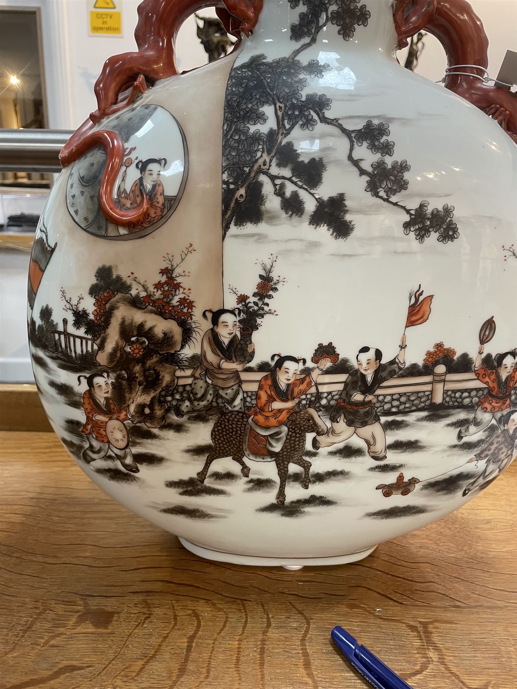 Chinese Republic period porcelain moon flask vase, of typical compressed spherical form, the neck and shoulders with applied iron red dragon handles, the body decorated in iron-red and grisaille with a 'one hundred children' design, depicting various children at play and engaged in musical pursuits within a garden setting, with apocryphal Qianlong mark beneath, H47cm