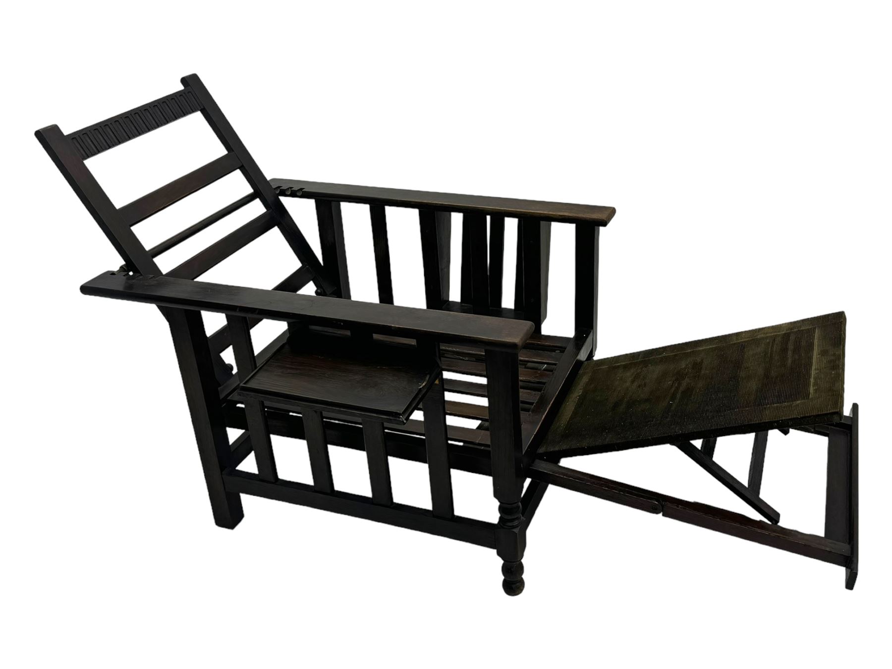 Late Victorian oak steamer chair, adjustable slatted backrest with grooved crest rail, wide armrests extending to a sliding adjustable footrest, open frame sides with vertical slats, side magazine rack and collapsible table, raised on turned front supports