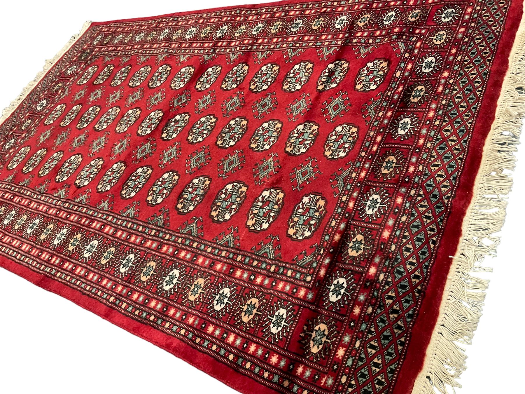 Persian Bokhara crimson ground rug, the field decorated with repeating Gul motifs and lozenges, the multi-band border with stylised plant motifs with black outlines