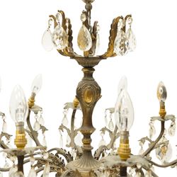 20th century Louis XV design gilt and patinated metal twelve-light chandelier, the foliate-cast baluster stem issuing scrolling acanthus branches with leaf-form drip pans, hung throughout with faceted glass pendants and lustre drops, suspended from chains beneath a foliate ceiling rose