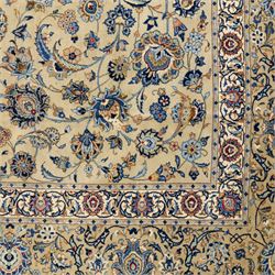 Persian Kashan carpet, beige ground, field with an all-over design of scrolling palmettes and floral sprays in blue and terracotta within a ivory ground and pale blue floral border