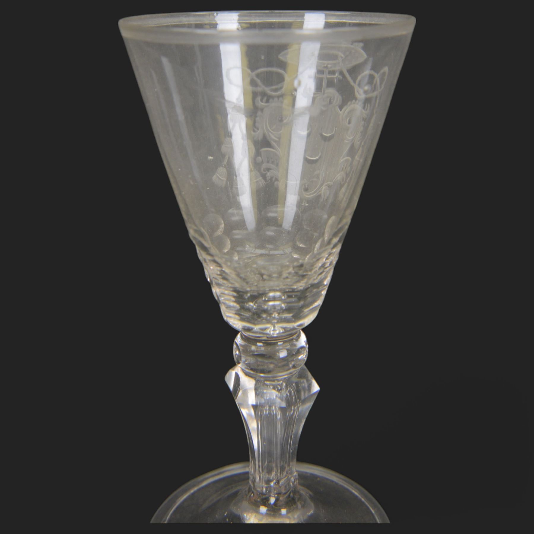 Two 18th century Continental facet cut drinking glasses, each with funnel bowl engraved with armorial type cartouche, upon a knopped and facet cut stem with internal elongated tear, and spreading folded foot, largest H15.5cm