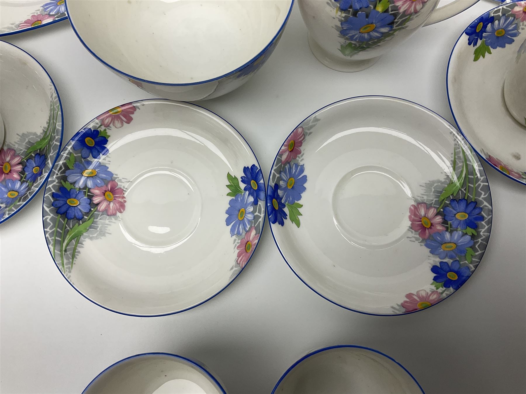 Shelley Strand shaped tea wares, decorated with blue and pink daisies upon a white ground, comprising four teacups, four saucers, three tea plates, milk jug, sugar bowl and cake plate, all with printed green mark beneath and painted pattern no 12216