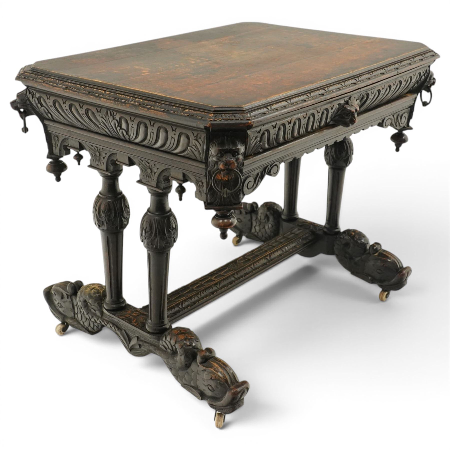 Victorian Jacobean Revival heavily carved oak centre table , rectangular top with canted corners and carved edge, fitted with single frieze drawer with central carved green-man handle with flanking gadrooning, the corners with lion masks, raised on fluted supports terminating to splayed stylised dolphin feet with castors, united by stretcher