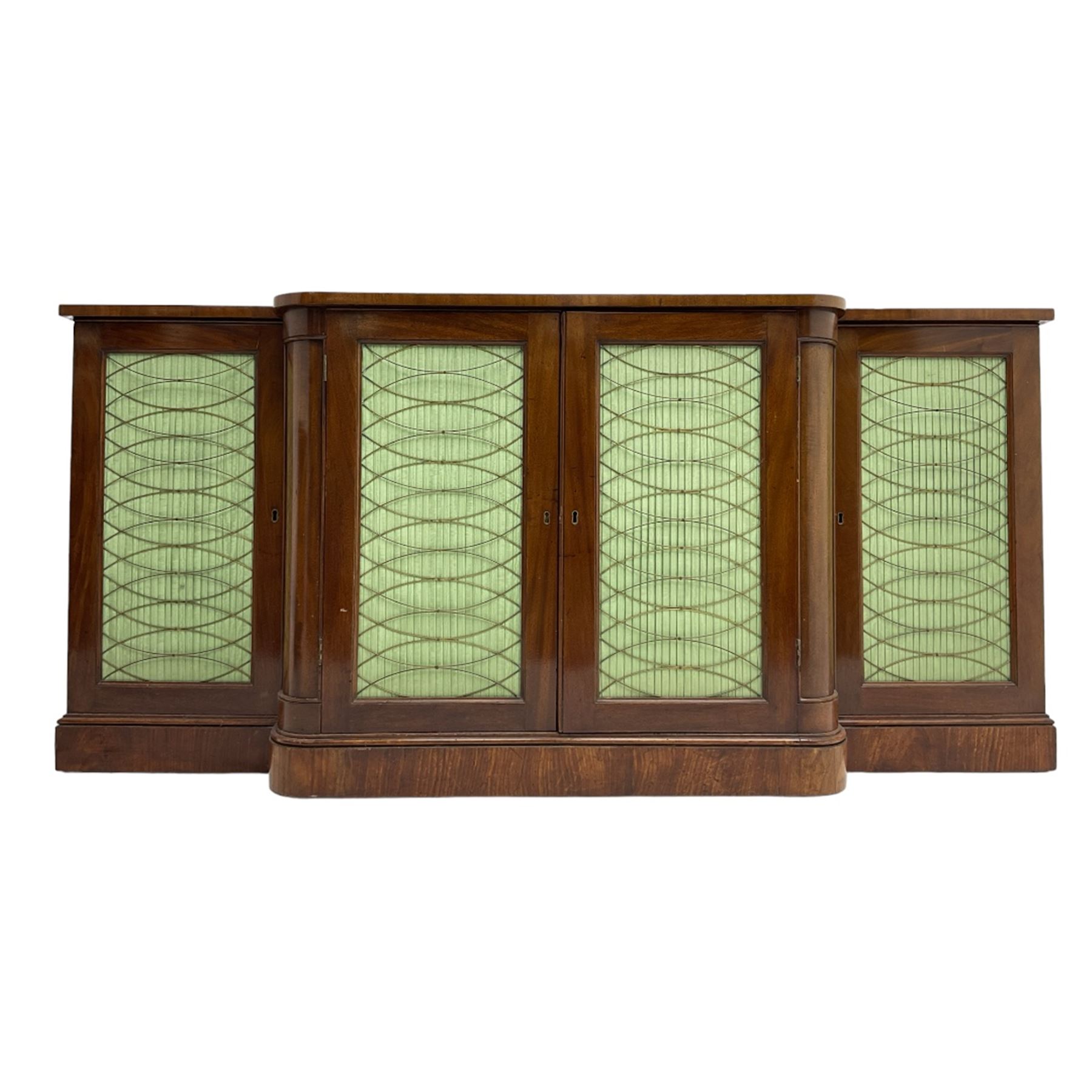 19th century mahogany break-front sideboard, raised brass gallery back with Greek key design, fitted with four cupboard doors, their pleated green fabric overlain with gilt metal grilles, lower moulded edge over plinth base