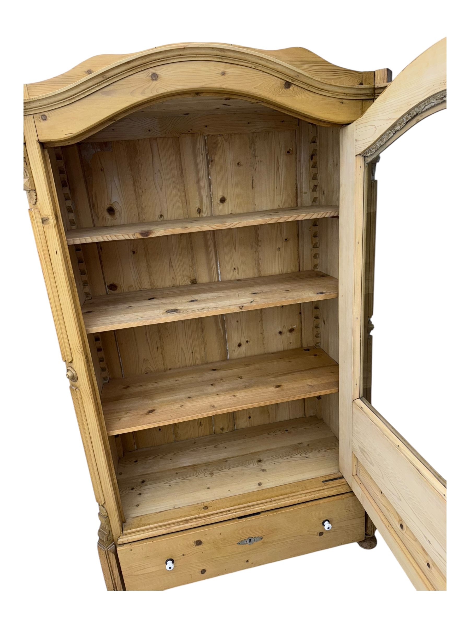 Late 19th century Continental pine vitrine, shaped and moulded arched cornice over a single glazed door enclosing adjustable shelves, flanked by carved pilasters with foliate and geometric motifs, fitted with single moulded drawer, raised on compressed bun feet