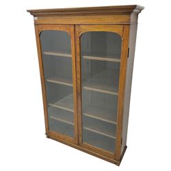 Victorian design oak display cabinet or bookcase, projecting cornice over two glazed doors, enclosing four adjustable shelves