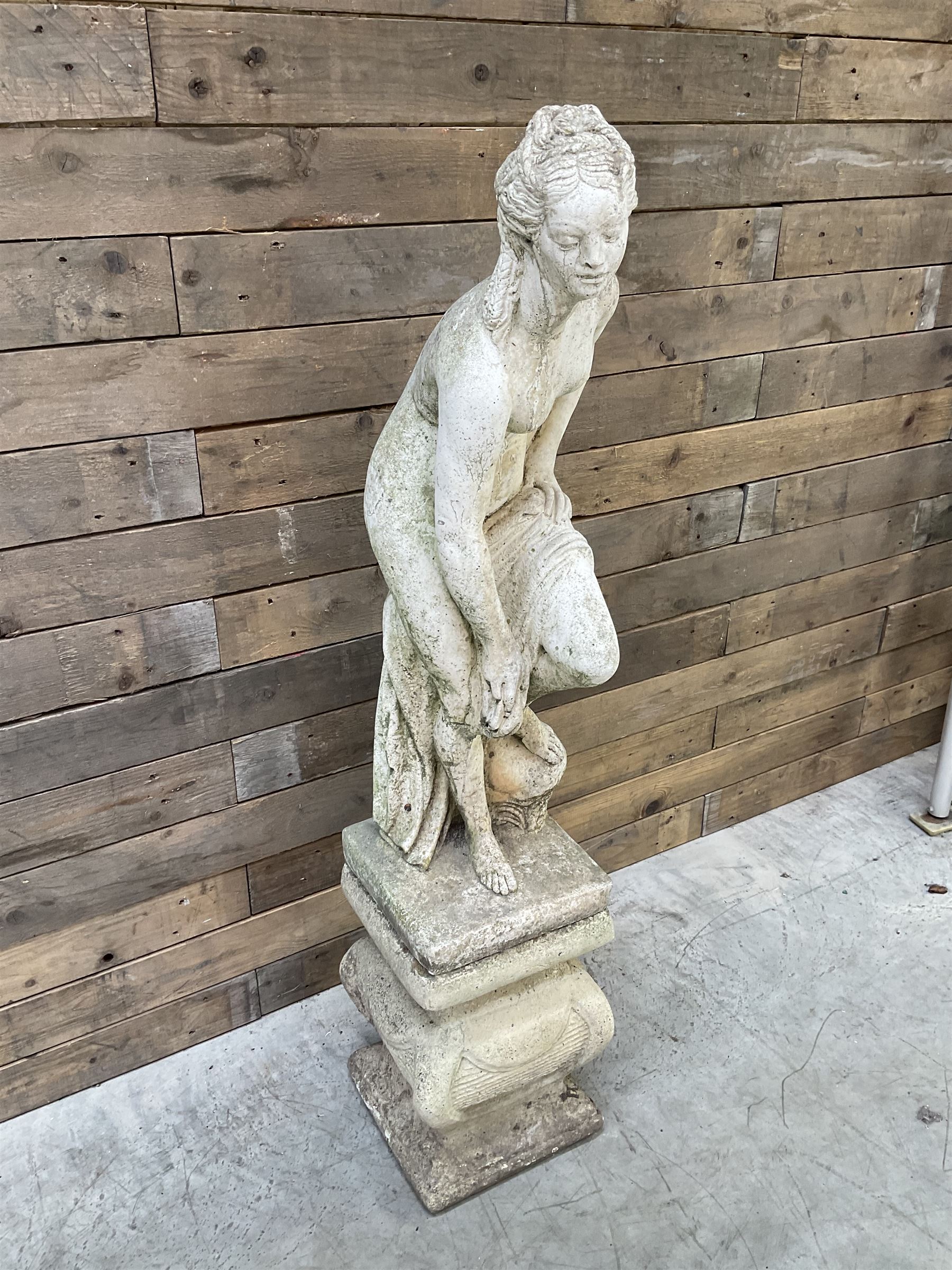 Cast stone garden statue of partially draped classical female figure on ornate pedestal 