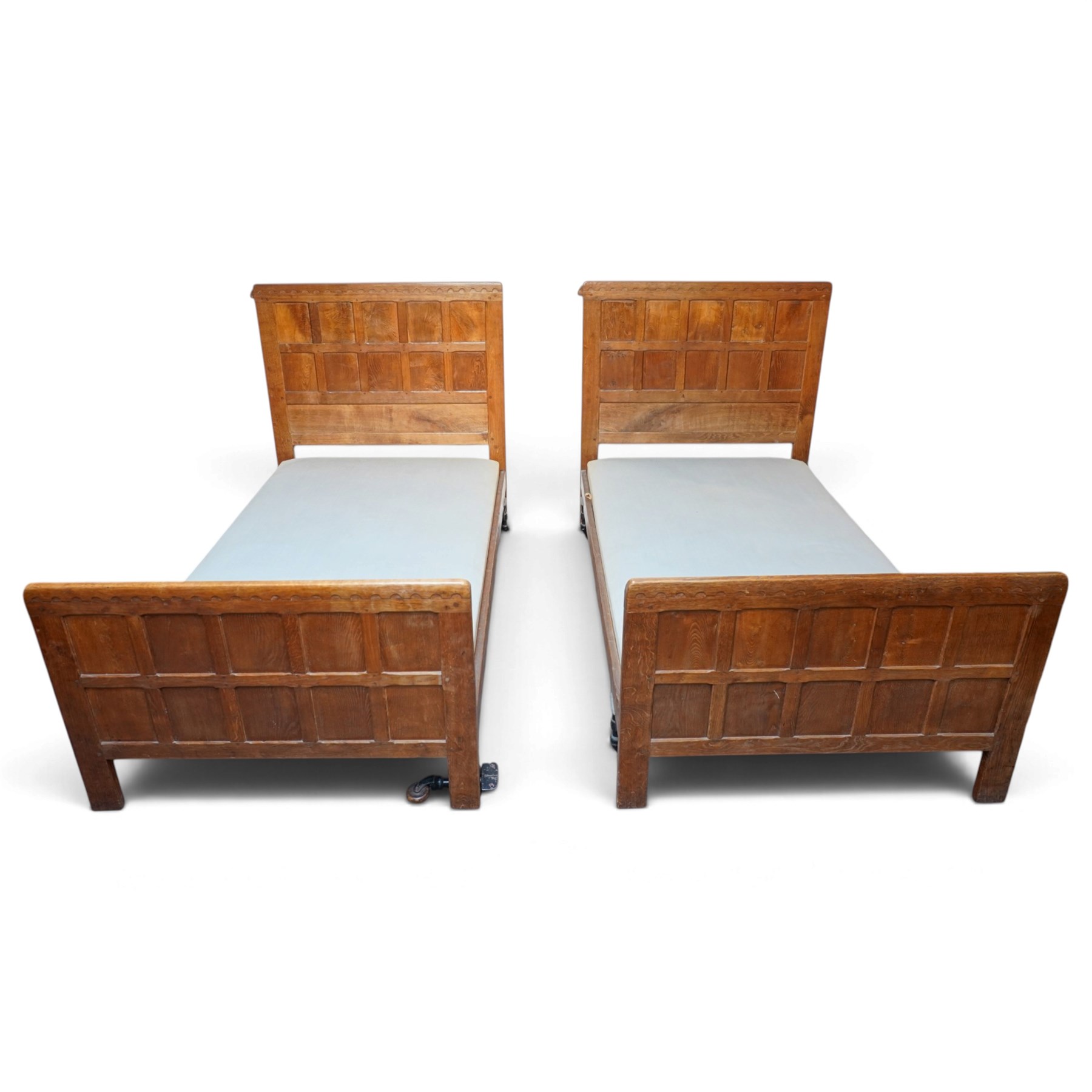 Mouseman - pair of 1930's adzed and panelled oak single beds, the head and foot-boards with arcade-carved cresting rails above adzed panels, with Vibase mattress supports, carved with mouse signature, by the workshop of Robert Thompson of Kilburn