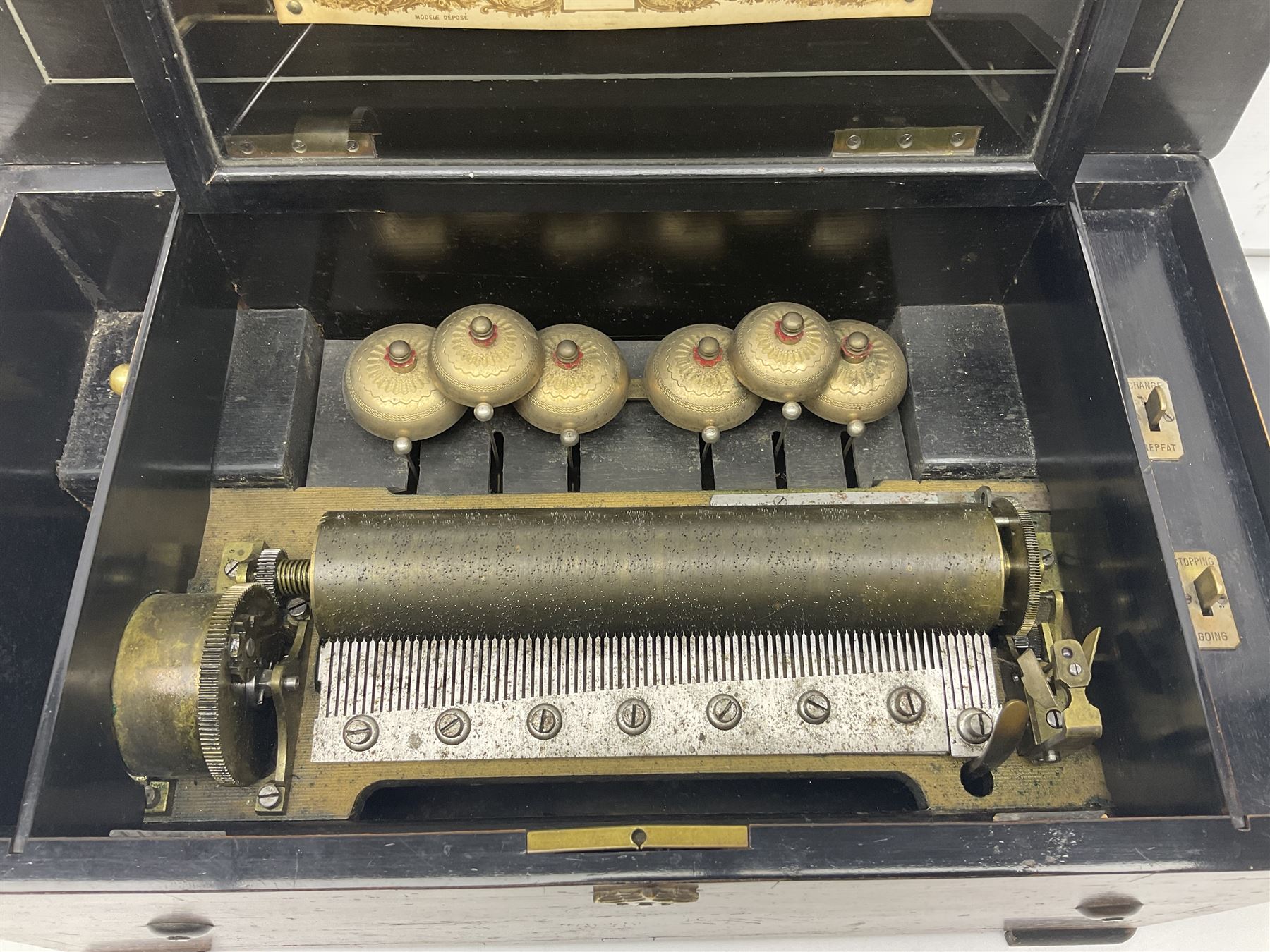 Large late 19th century Swiss bells-in-sight musical box with 27.5cm cylinder playing eight airs on a 27cm two-piece comb with seventy-seven teeth and six graduated engraved saucer bells with strike/silent facility; in crossbanded rosewood and ebonised case, the front and hinged lid inlaid with musical trophies, opening to reveal a song card under the lid and hinged glazed cover to the movement; serial no.7539 L53cm