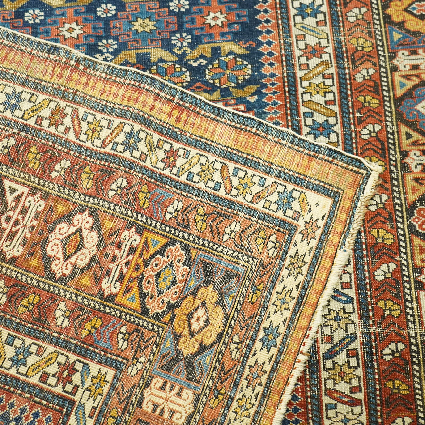 Two antique Caucasian Shirvan rugs, indigo field decorated with horizontal bands of small geometric floral and star motifs within multiple finely drawn borders featuring diamonds, rosettes, and stylized leaves in a palette of madder red, ivory, ochre, and pale blue, with fringe ends, 195x137cm, together with a similar smaller rug, 143x96cm