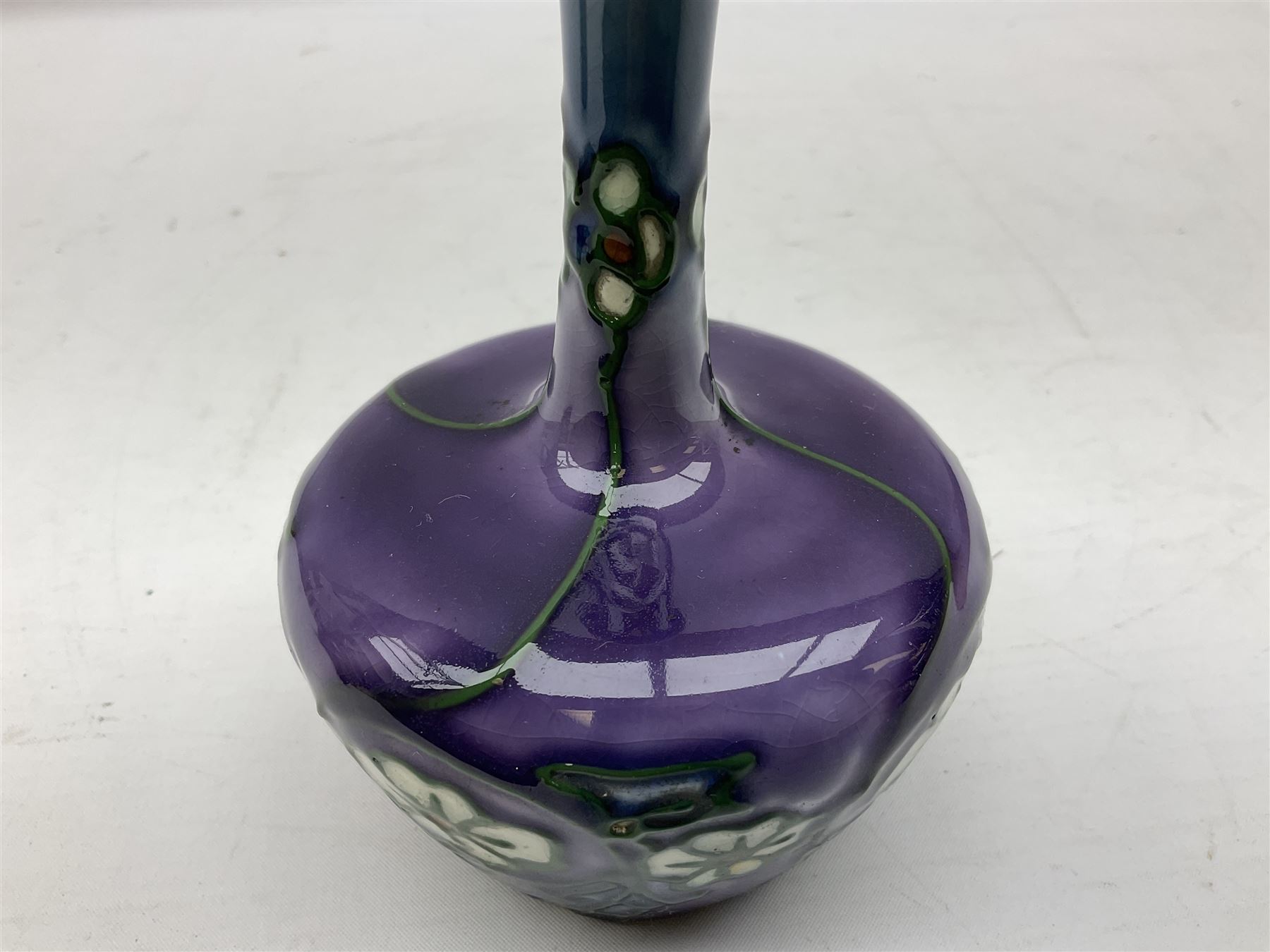 Three Minton Secessionist vases, with tube-lined stylised flower decoration, two upon a red ground and third upon a purple ground, all with printed mark to base 'Minton Ltd, No. 33', H13cm