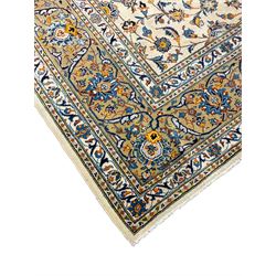 Persian Kashan ivory ground carpet, the field decorated with trailing foliate branches and stylised flower head motifs, guarded border with repeating design decorated with scrolling leafy branch and plant motifs 