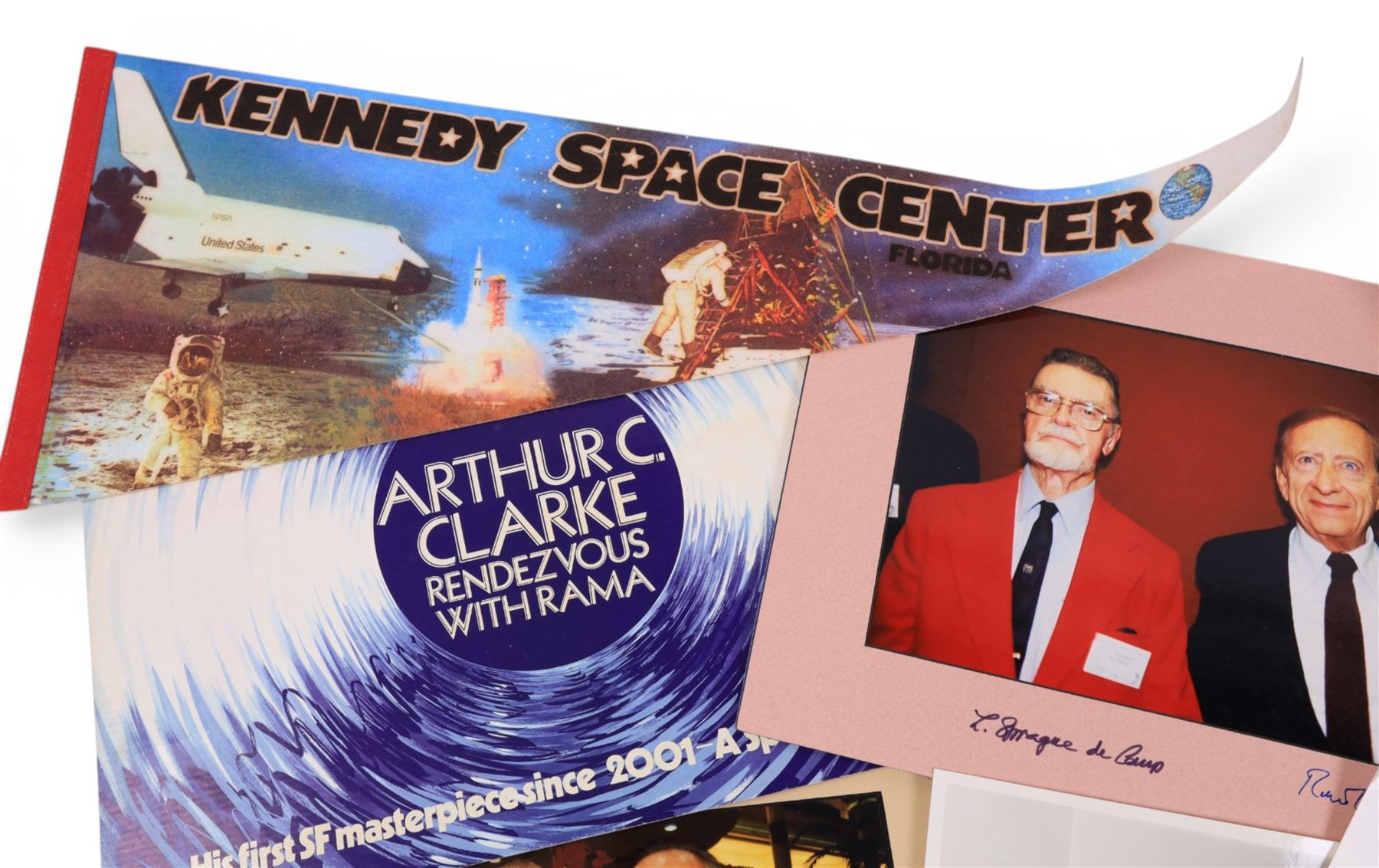 Collection of ephemera relating to Arthur C Clarke, including colour photograph of Arthur with author Joe Green, Jay Kubica and astronaut Chris Hadfield at NASA Kennedy Space Centre, Kennedy Space Centre pennant flag, colour photographs of authors Sam Moskowitz with Forrest Ackerman and L. Sprague de Camp with Robert Bloch, all signed below by the authors, a black and white photograph of Arthur for his 13-Part ITV series 'Arthur C Clarke's Mysterious World', Pan Books cardboard advertisement for Rendezvous with Rama and an Evening Standard poster for The Other Side of the Sky

Notes: This item is from the private collection of Arthur C. Clarke's brother.
