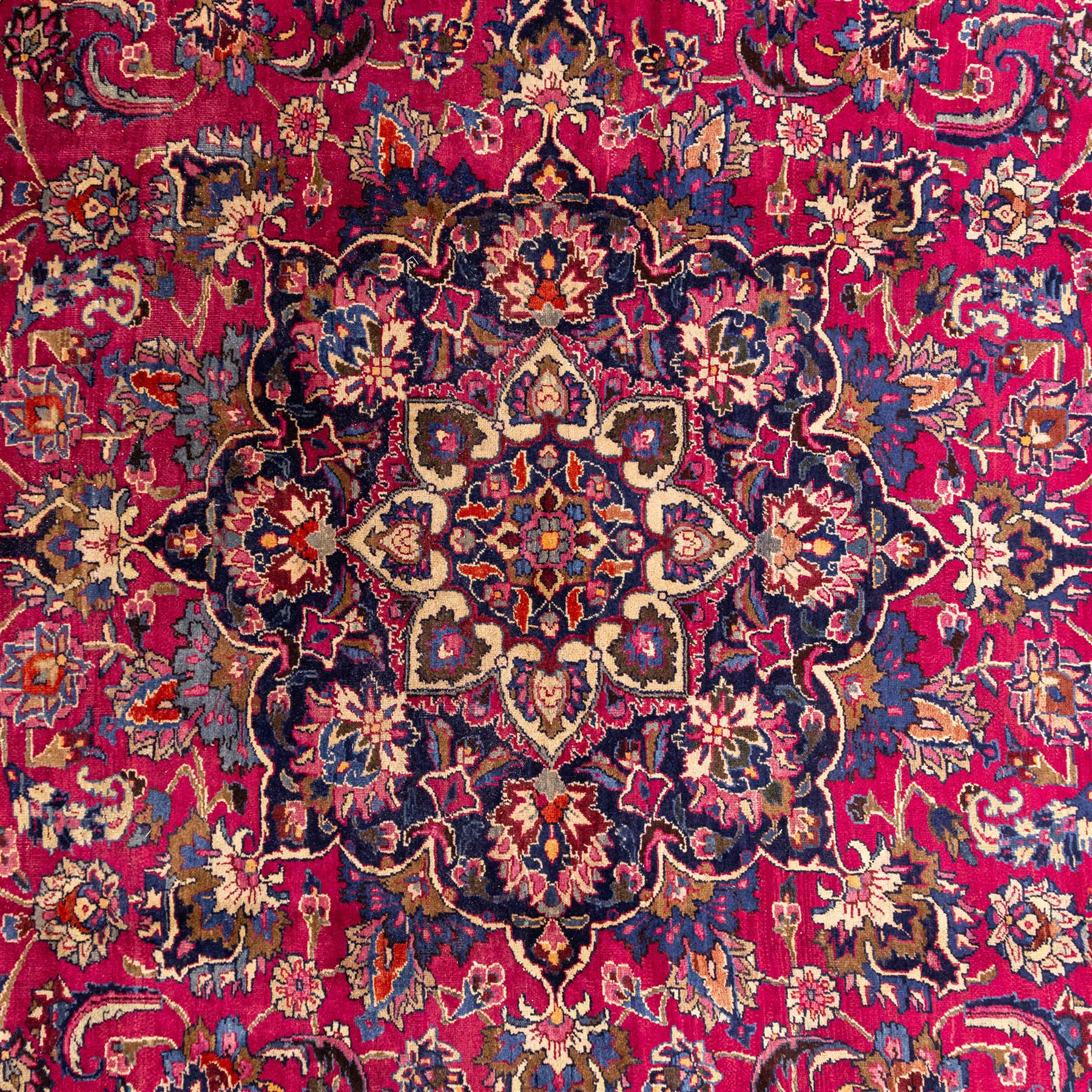 North East Persian Mashad hand-knotted carpet, rich madder red field with central cusped foliate medallion with issuing scrolling arabesques, palmettes, and floral sprays, enclosed within a broad indigo main border of bold palmettes, between multiple guard stripes, with cotton fringe ends 