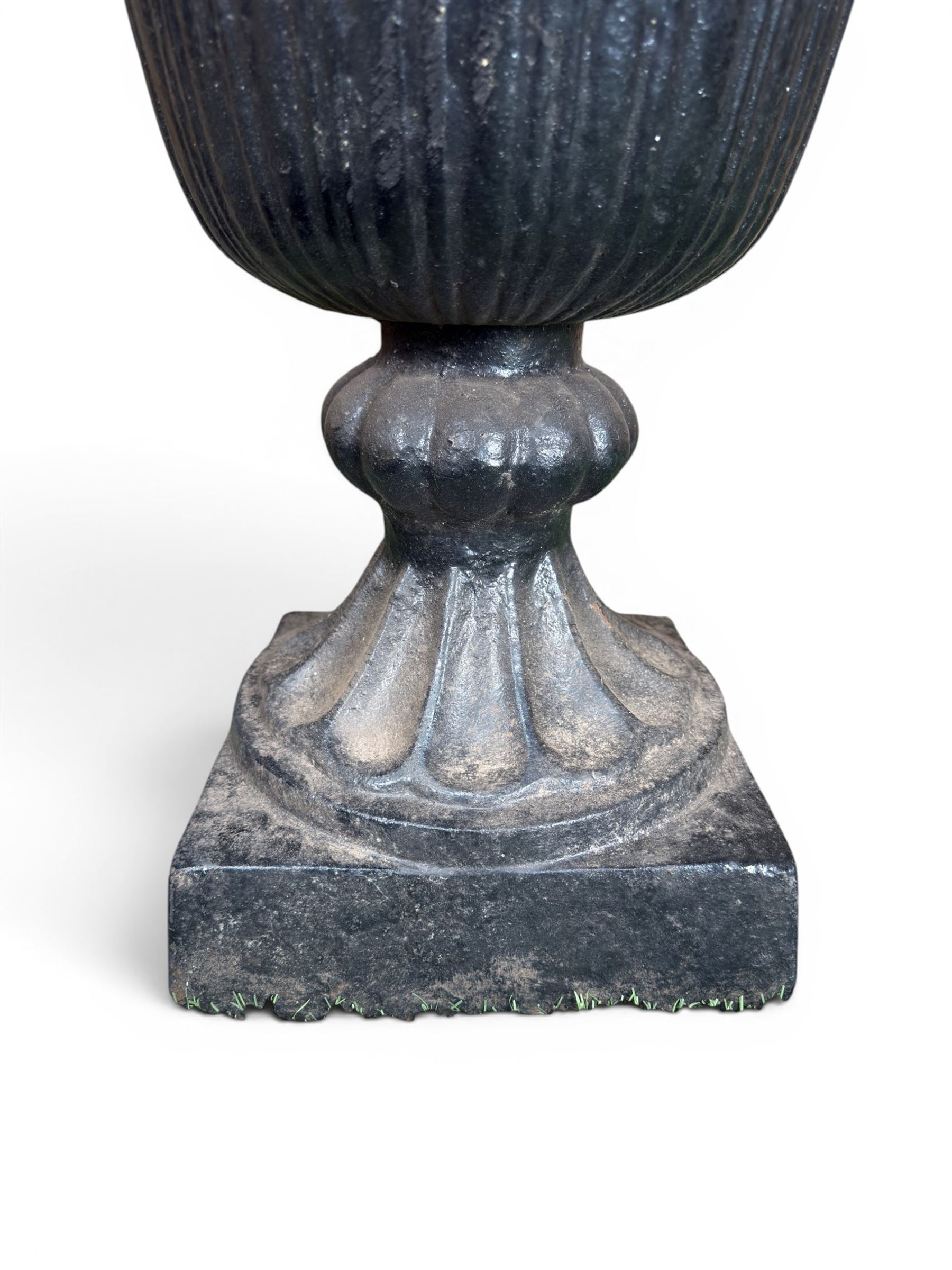 Pair of Victorian large scale cast iron garden urns, flared petal shaped rim with tapering waist, gadrooned base on square plinth, finished in black paint