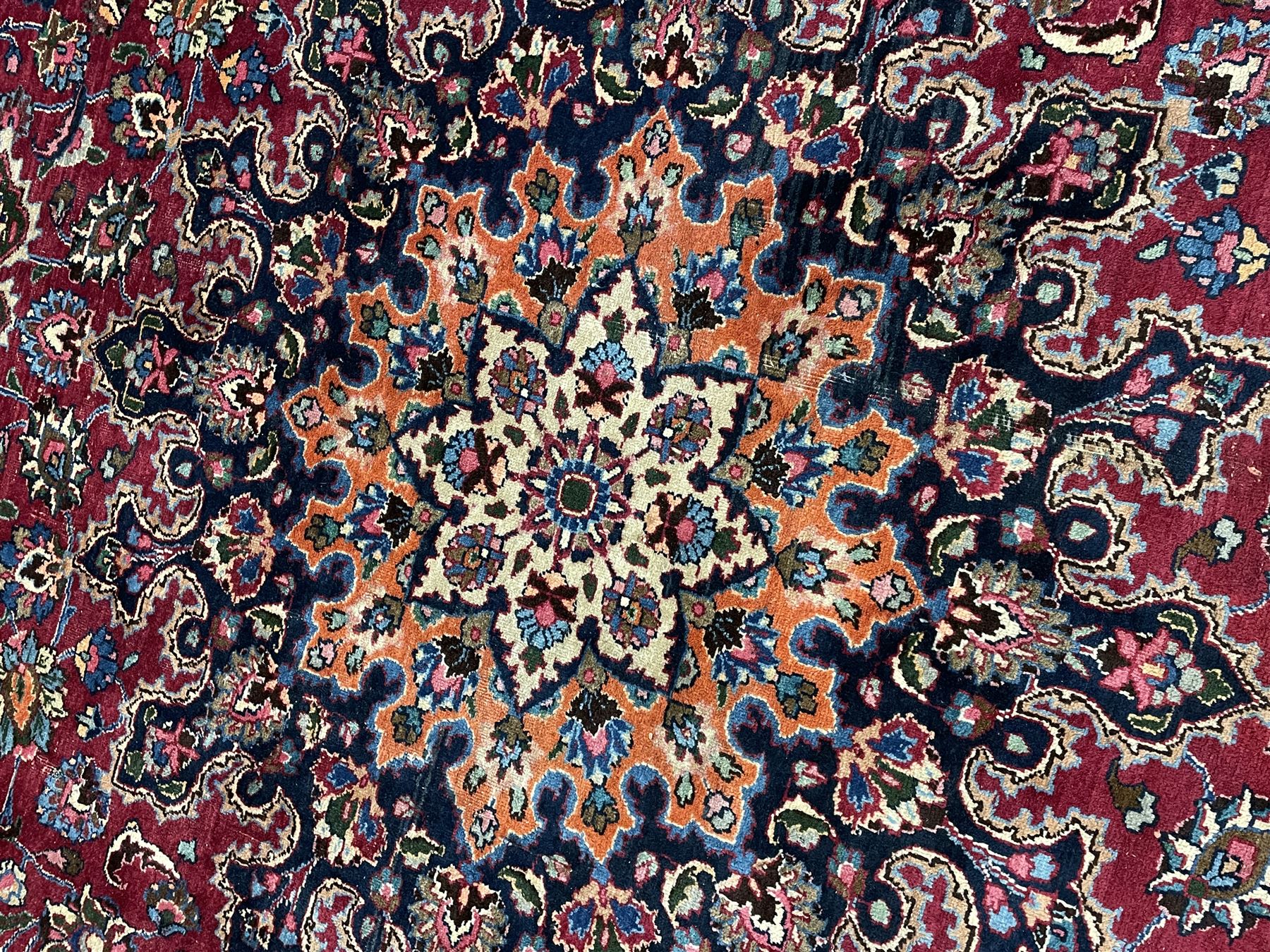 Persian Meshed carpet, plum ground and decorated with stylised flower heads and interlacing foliate, large central stylised medallion with orange detail, the orange mirrored in the five band border decorated with scrolling floral design, signature panel to end 