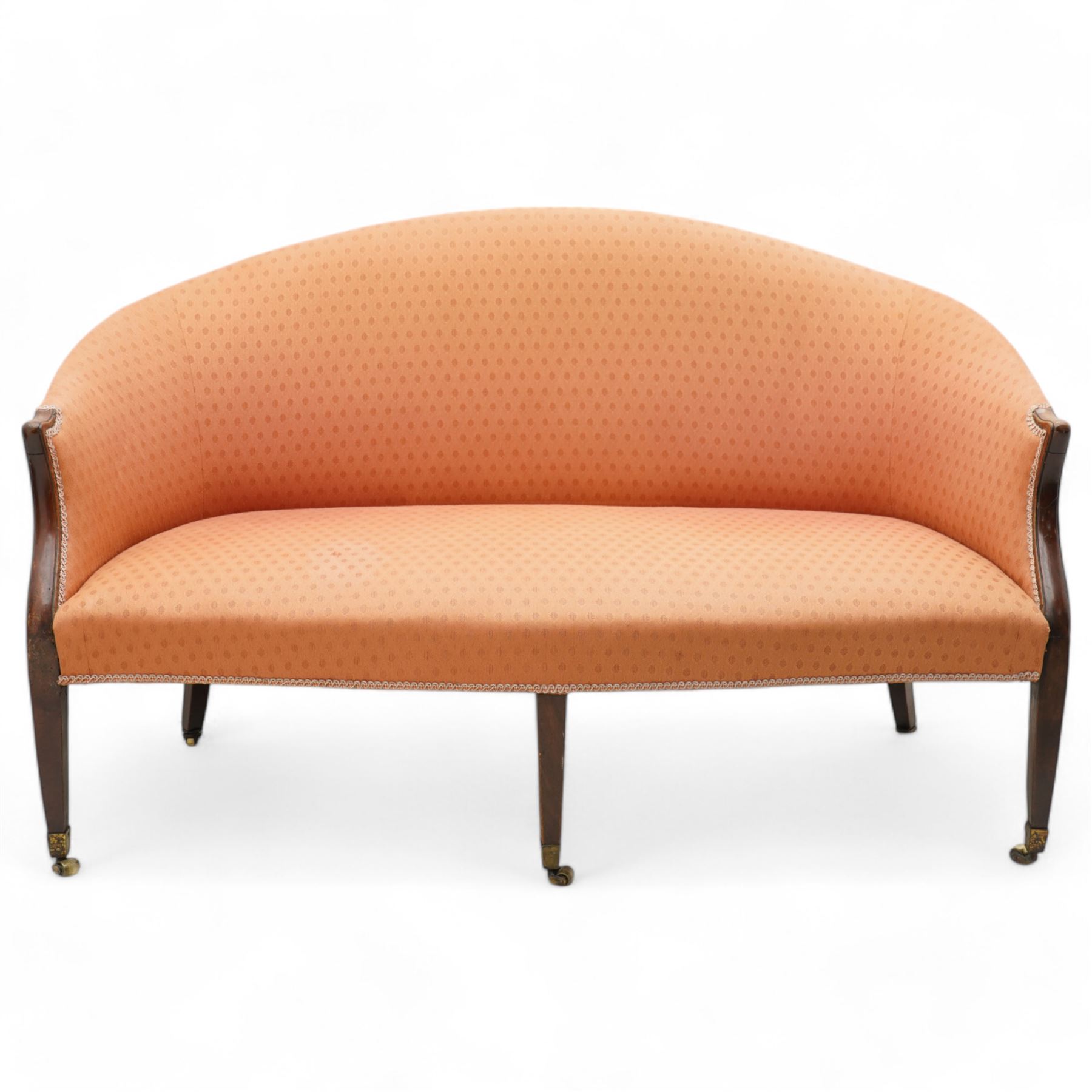 George III Hepplewhite design settee, arched back over serpentine set, upholstered in salmon fabric with repeating pattern, on square tapering supports with brass cups and castors 