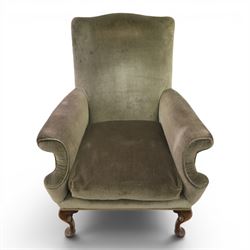 Pair of Georgian style wing armchairs, upholstered in green velvet, each with shaped wing backs, padded scroll arms and loose seat cushions, raised on cabriole supports terminating in pad feet, one with tasselled fringe