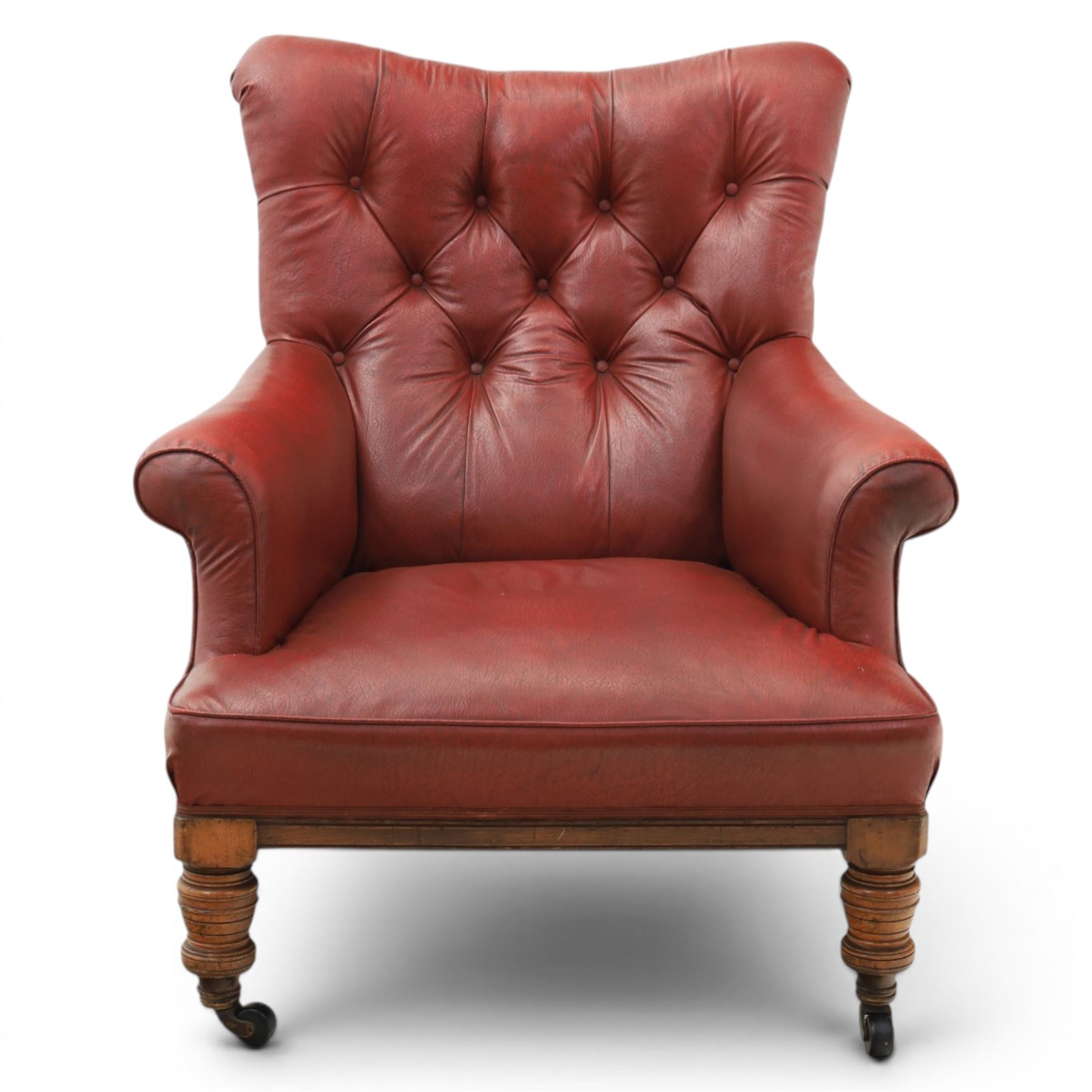Early 20th century style oxblood red leather Chesterfield armchair, deep buttoned shaped back over padded scroll arms and loose seat cushion, raised on turned mahogany front supports with brass caps and castors