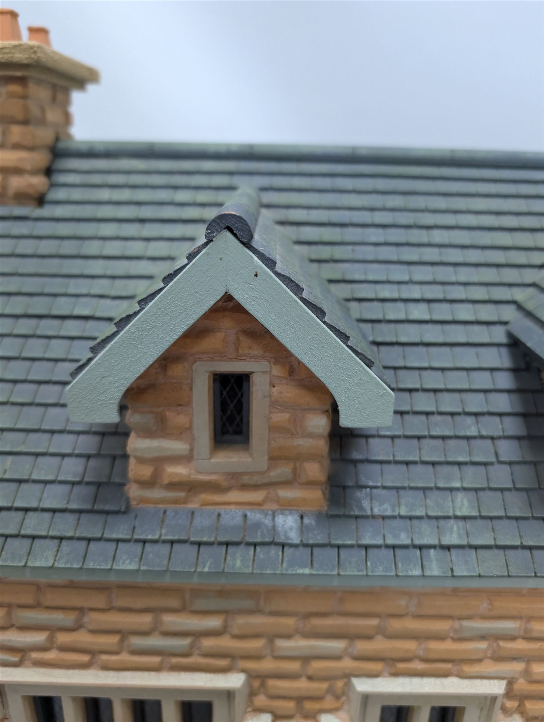 1:24 scale stone effect three-storey cottage dolls house, with green arched door and lattice effect windows, decorated to the interior with wooden floors, wired lighting and fire places, H45cm, W57cm, D26cm