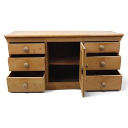Victorian stripped pine sideboard, rectangular plank top rounded edges, with central cupboard door with shaped panel, flanked by two banks of three graduating drawers with turned knobs, raised on a plinth base 