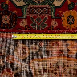 North Persian crimson ground rug, the field densely decorated with stylised flowering plants, urns and polychrome rosettes, within a stepped ochre outline, dark ground floral spandrels and geometric side panels