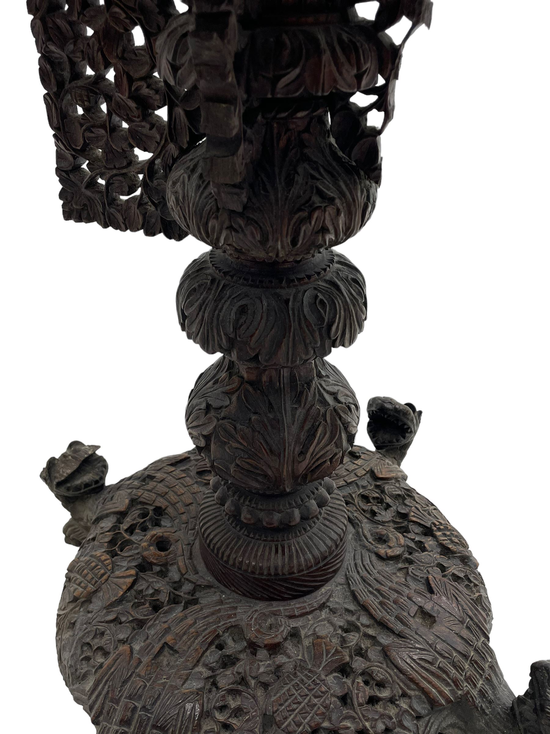 Late 19th century Anglo-Indian carved hardwood occasional table, circular tilt-top carved profusely with mythical animals and foliage decoration, pierced and carved with interlaced leafy branches, leaf carved pedestal supports on a raised platform with further carved and pierced foliage decoration, four carved feet in the form of mythical beasts with gaping jaws 