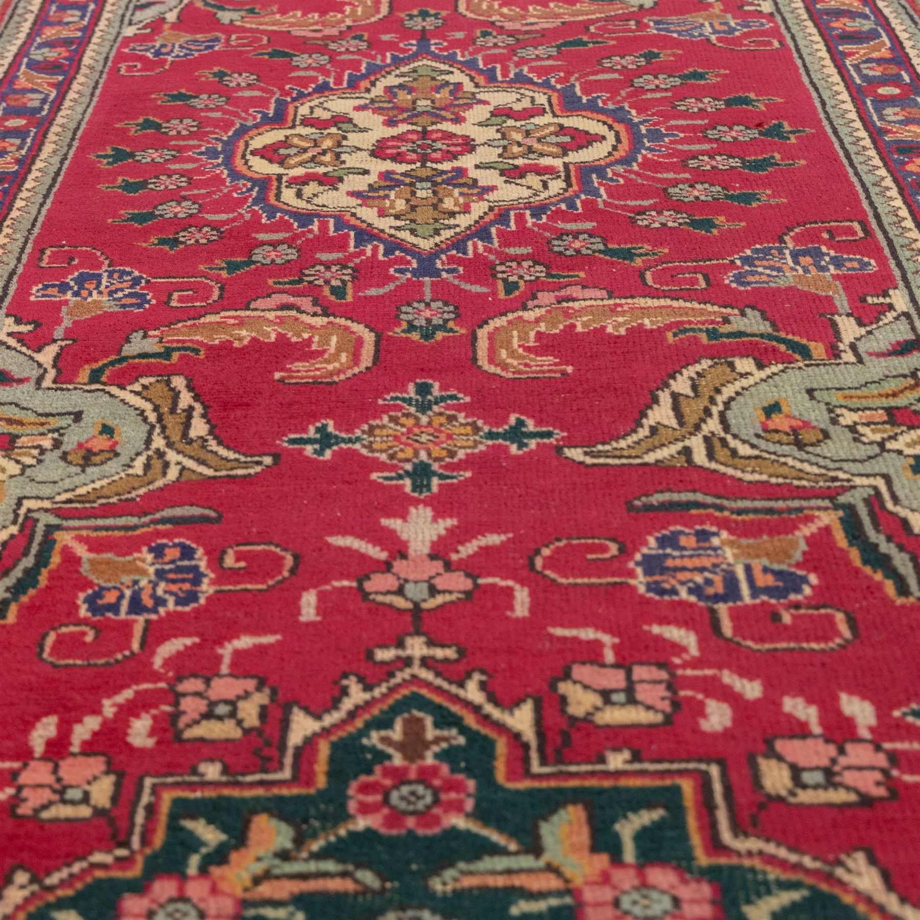 North West Persian Tabriz hand-knotted runner, madder red field with central octagonal medallions of sage green, navy and ivory, ground enclosing a floral rosette and radiating angular vinery, scrolling floral sprays and palmettes either end with shaped pendants principal border on navy ground decorated with a continuous vine-scroll of palmettes and rosettes, flanked by narrow guard borders, with cotton fringe ends 