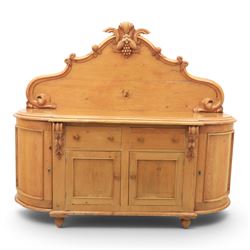 Victorian pine chiffonier, shaped moulded top with raised scroll carved back surmounted by carved fruit and foliate crest, fitted with two frieze drawers over two panelled cupboard doors, the outer cupboards of bowed form, carved foliate corbels, on plinth base